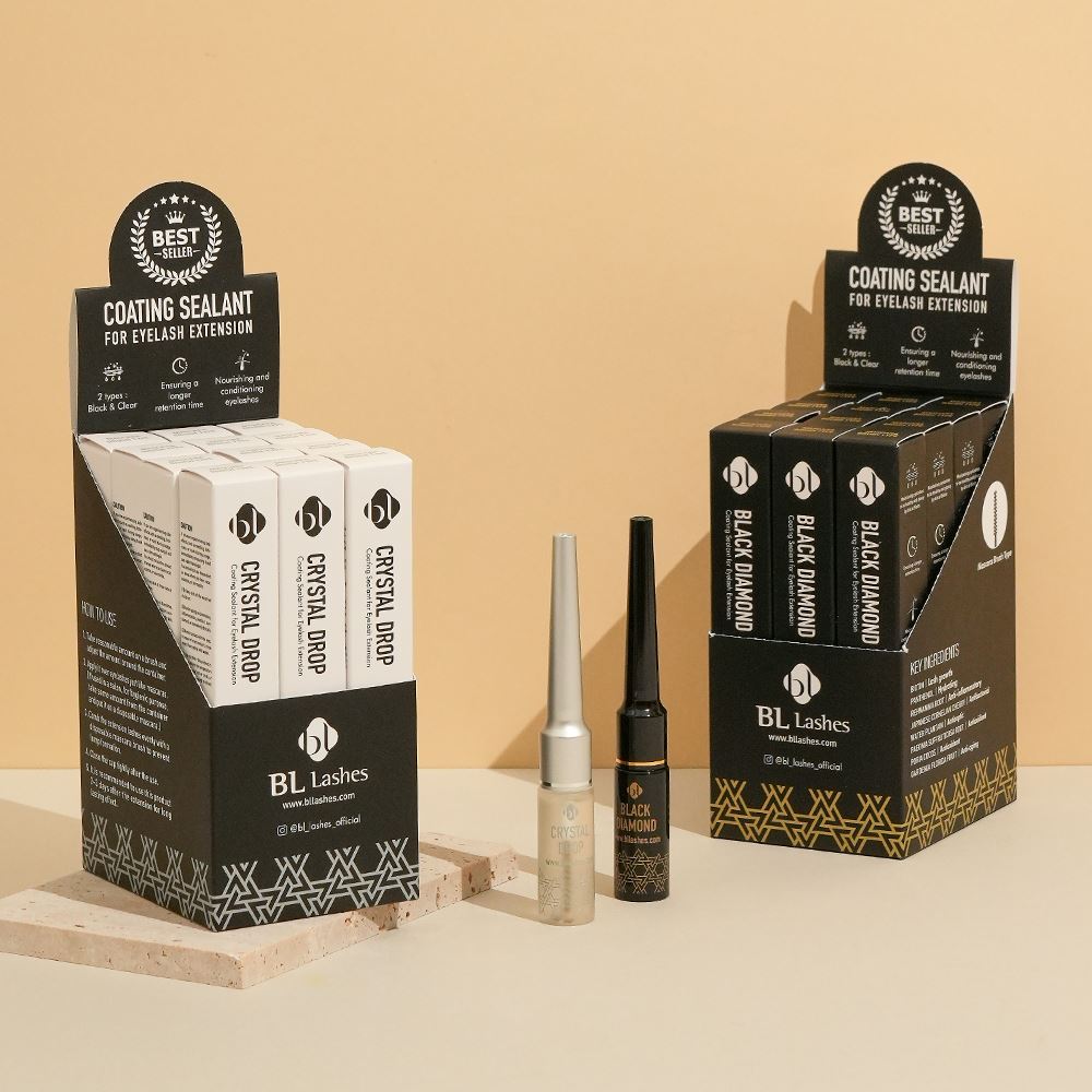 Retail display boxes and bottles of BL Lashes Crystal Drop and Black Diamond Coating Sealants for eyelash extension, arranged on textured stone blocks.