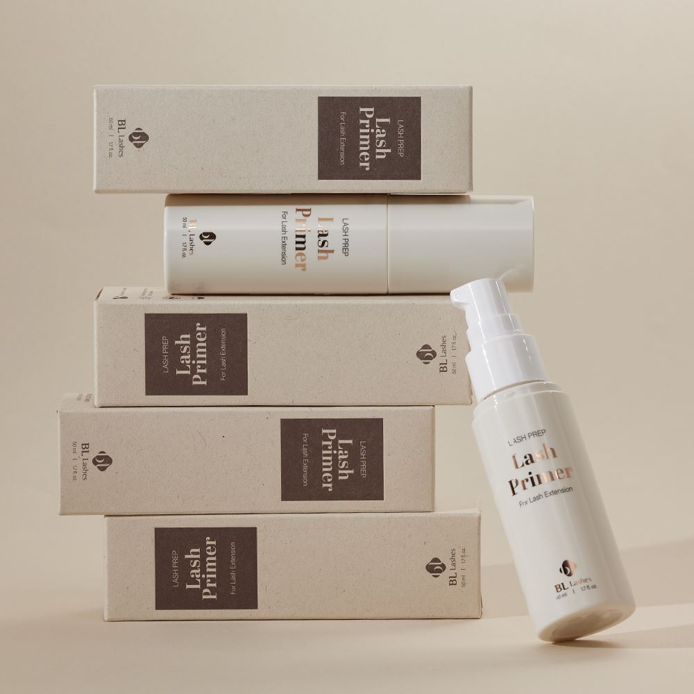 BL Lashes Lash Prep Lash Primer bottles and stacked packaging boxes, featuring one open bottle with a white pump dispenser leaning against the stack.